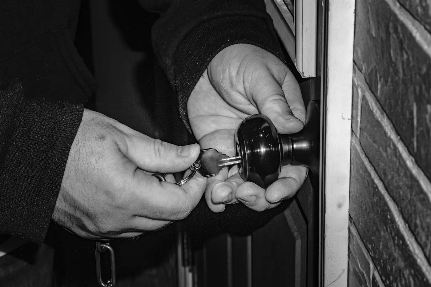 Mains insérant une clé dans la serrure d'une porte, en noir et blanc